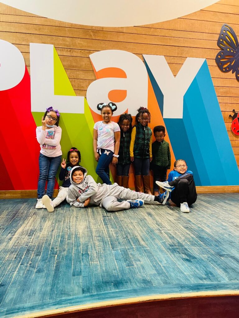 Children posing in front of large sign that signs "play"